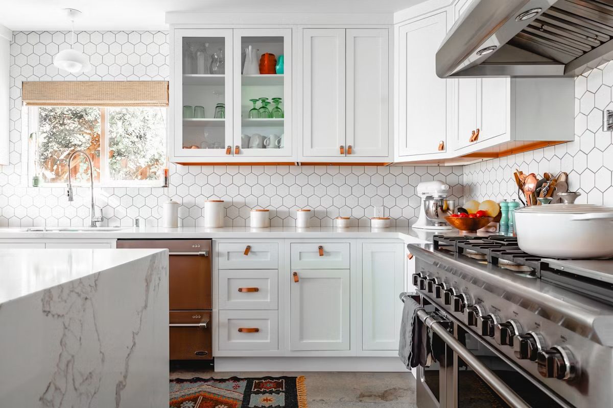 A white kitchen with hexagon tile, glass cabinets, and leather pulls